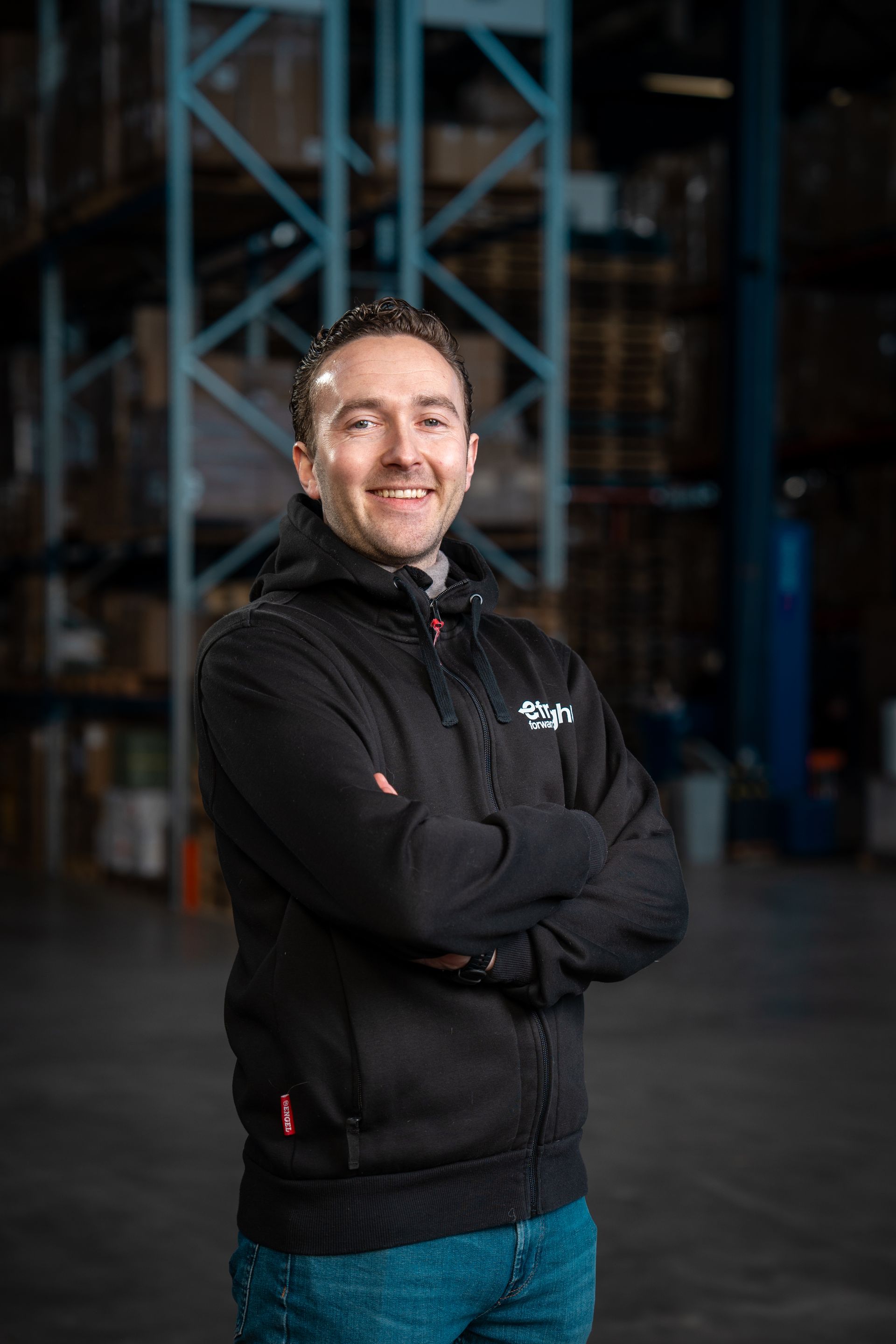 een man staat met zijn armen over elkaar en glimlachend in een pakhuis.