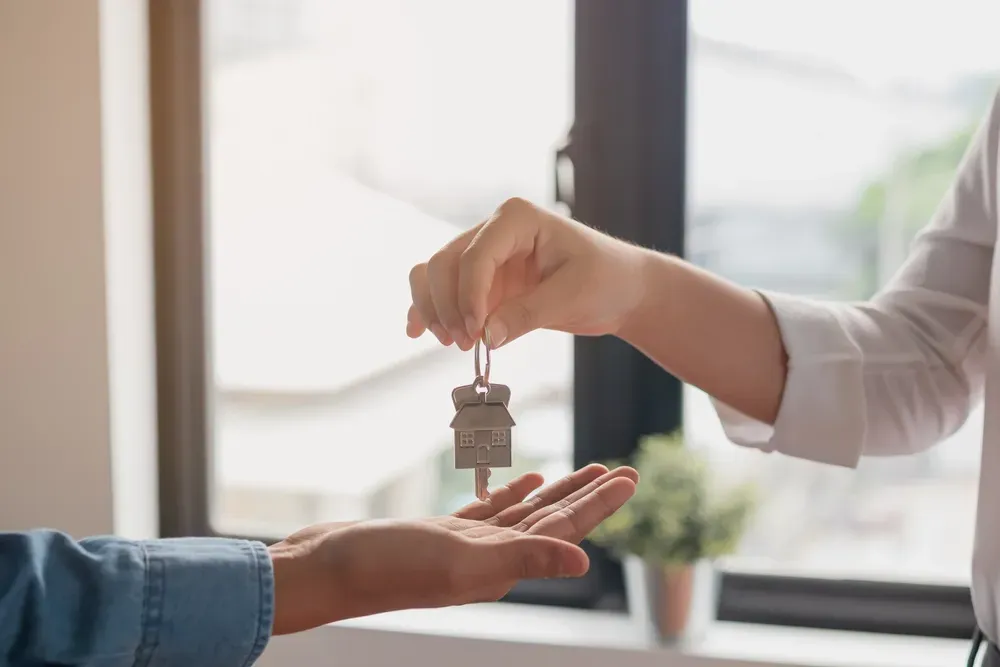 A person handing a house-shaped key to another person, symbolizing a new home or real estate transaction. — Diamond Real Estate QLD in Burpengary, QLD