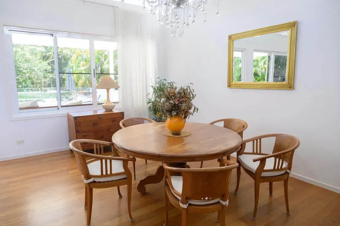 Dining Room With Wooden Table, Chairs, Mirror, and Window With Greenery — Diamond Real Estate QLD in North Lakes, QLD