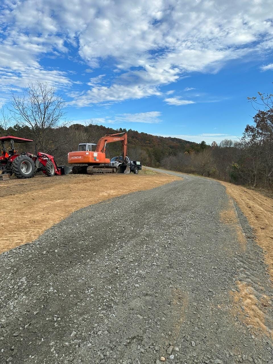 A tractor and an excavator are parked on the side of a gravel road - Alexander, NC - Land Solutions, LLC