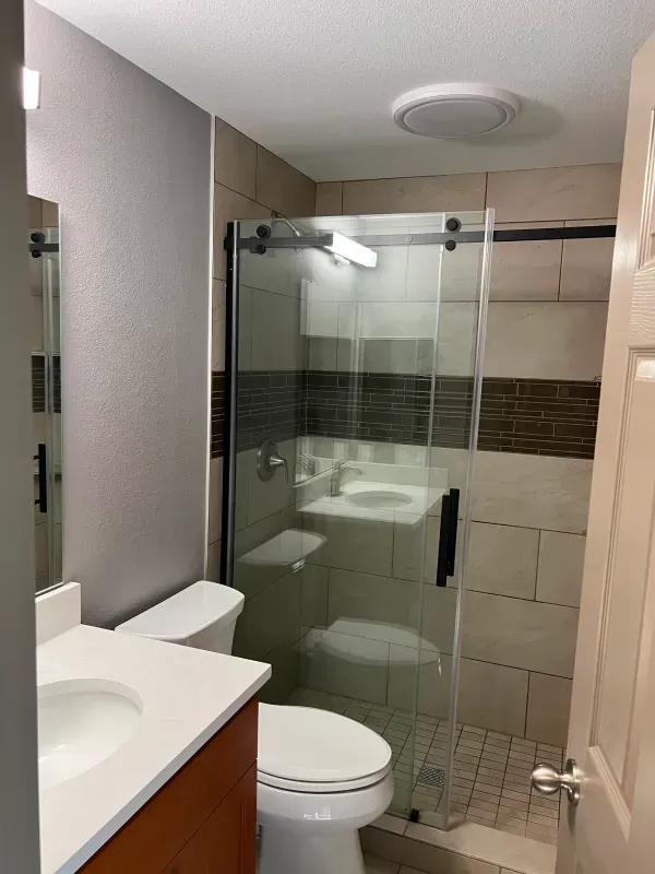 Bathroom with a toilet, vanity, and glass shower. Light-colored tile and walls.
