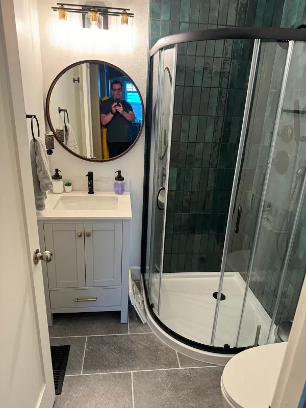Small bathroom with grey vanity, curved shower, and dark green tiled wall.
