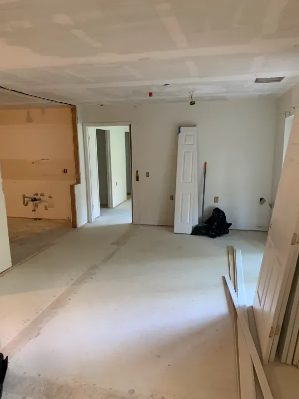 Interior room under construction with drywall and materials, white walls, and open doorways.