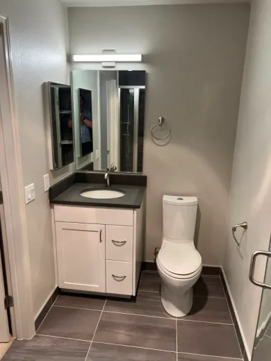 Bathroom with white vanity, toilet, dark countertop, gray walls, and dark tiled floor.