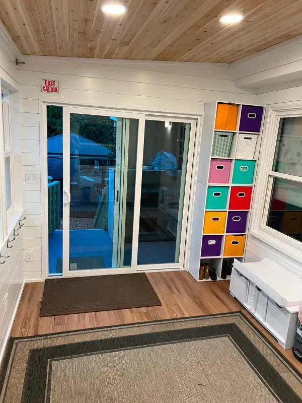 A bright sunroom with sliding glass doors, colorful storage cubes, and a welcoming entry rug.