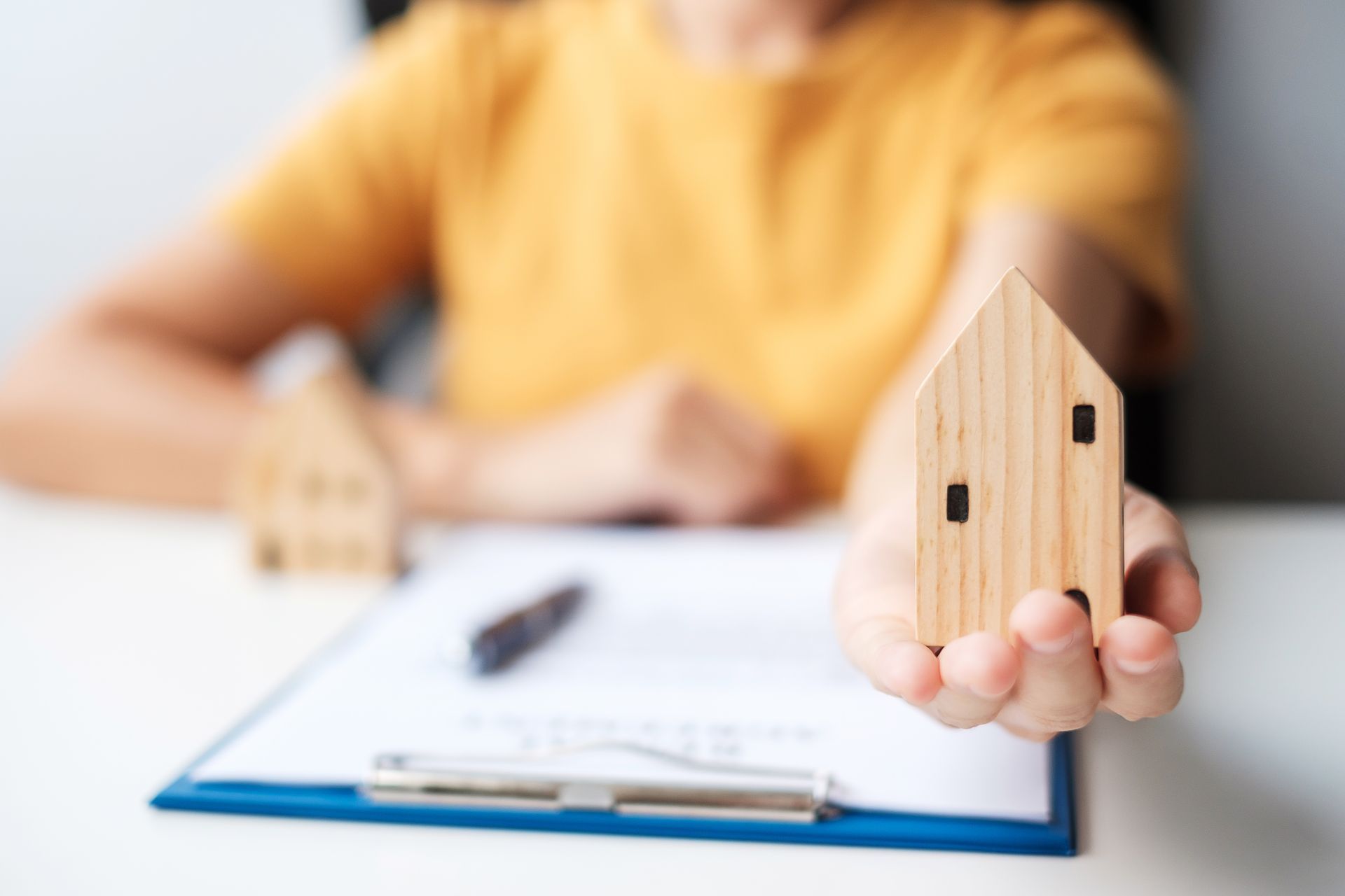 A person is holding a small wooden house in front of a clipboard.