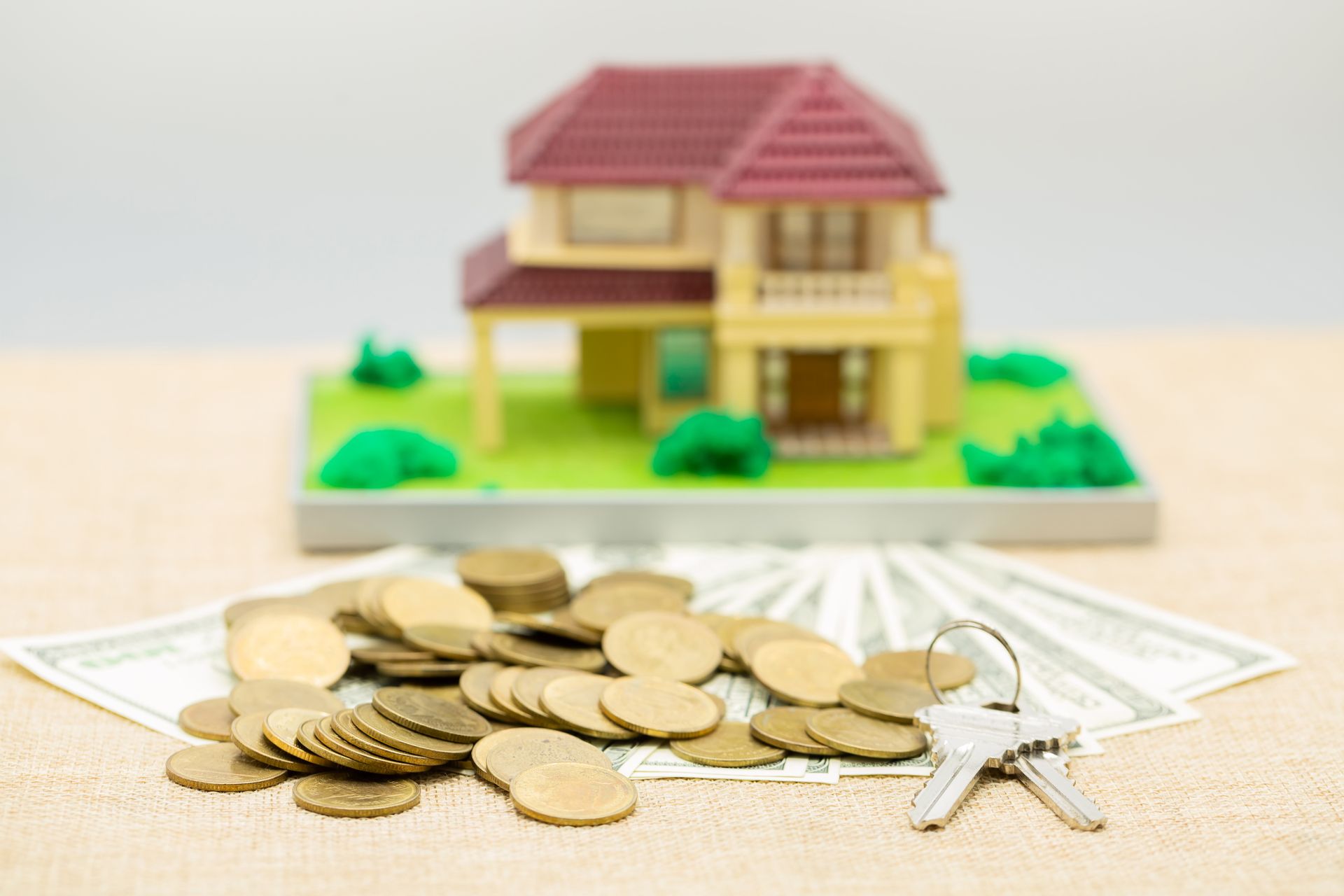 A model house is sitting on top of a pile of money and coins.
