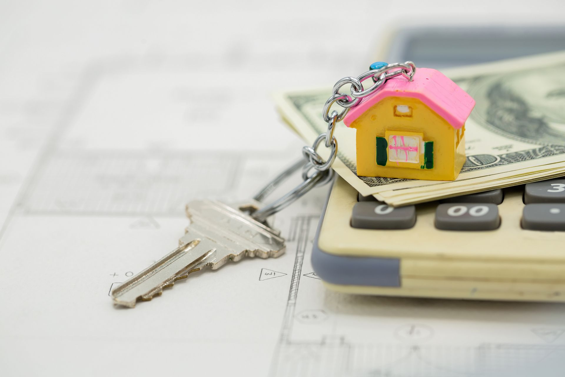 A key and a house keychain are sitting on top of a calculator.