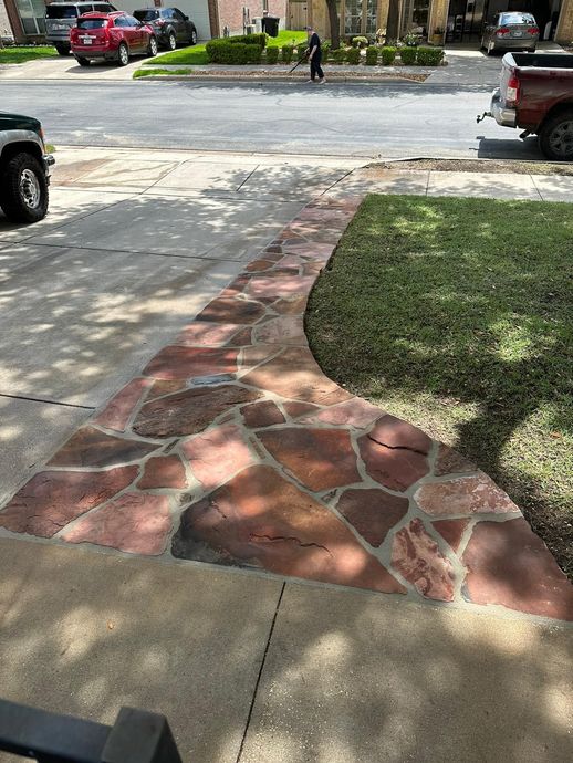 A stone-paved walkway curves along a green lawn, bordering a concrete driveway and residential street.