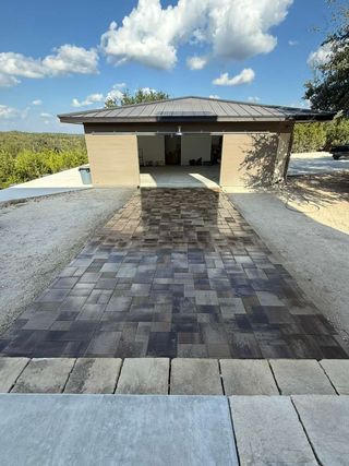 A stone paver walkway leads to the entrance of a neutral-colored garage set against a sunny, outdoor landscape.
