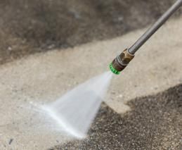 A person is using a high pressure washer to clean a concrete floor.