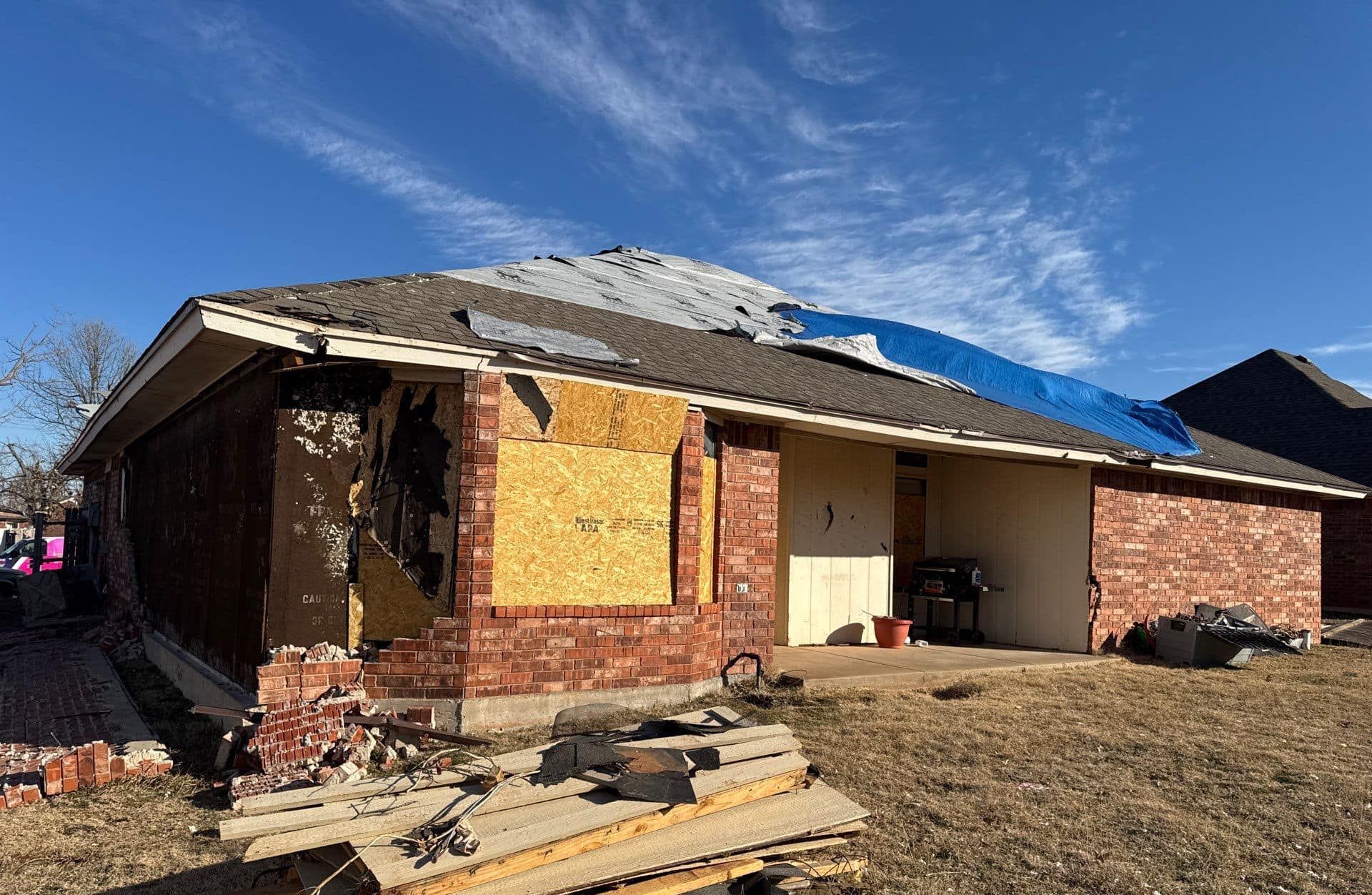 A brick house with a blue tarp on top of it.