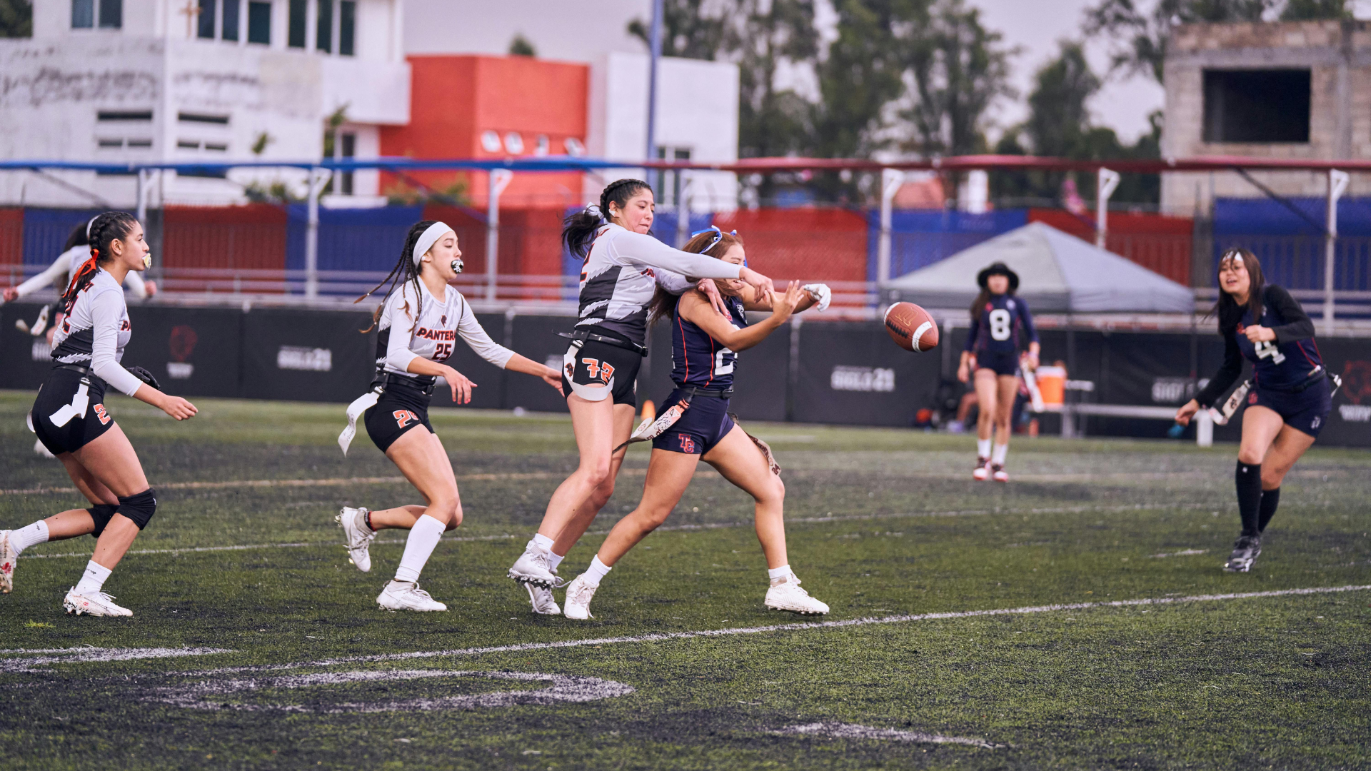Three women running through agility ladder drills on a grassy field. They wear athletic clothes and have flags attached.