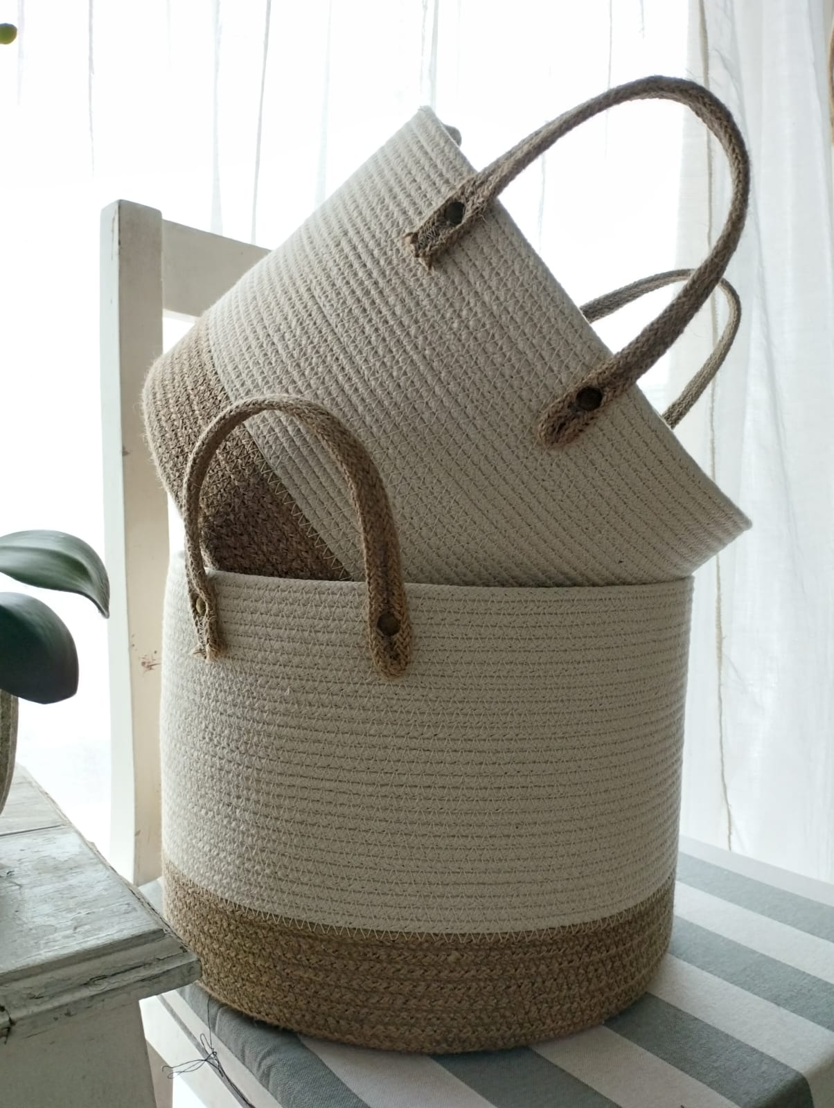 Dos cestas de almacenamiento tejidas de color beige apiladas junto a una ventana luminosa.