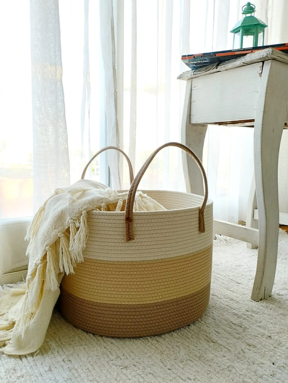Cesta de mimbre con manta color crema junto a una mesa blanca en una habitación luminosa y espaciosa.
