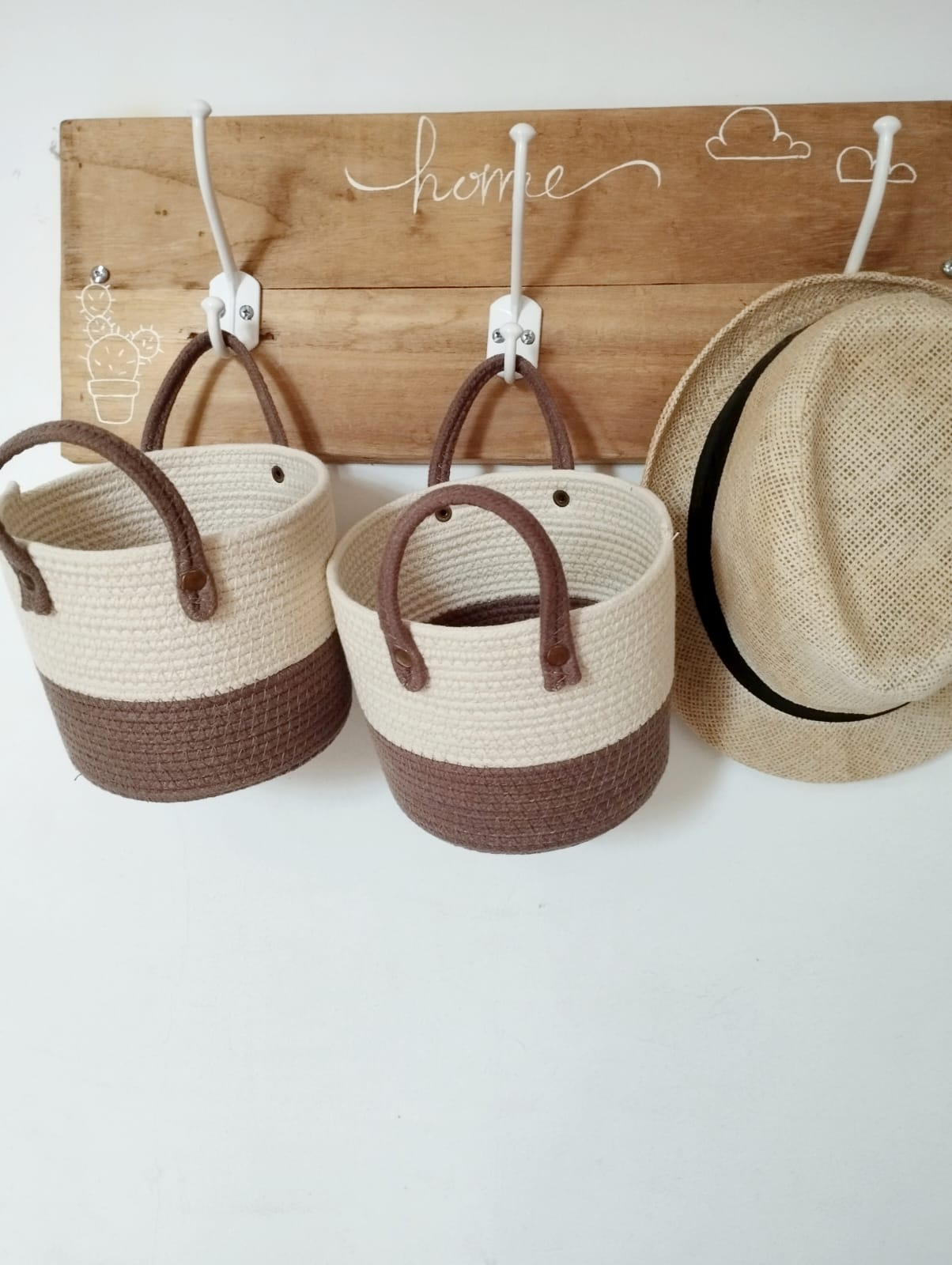 Tres cestas colgantes de mimbre y un sombrero de paja sobre una tabla de madera con ganchos.