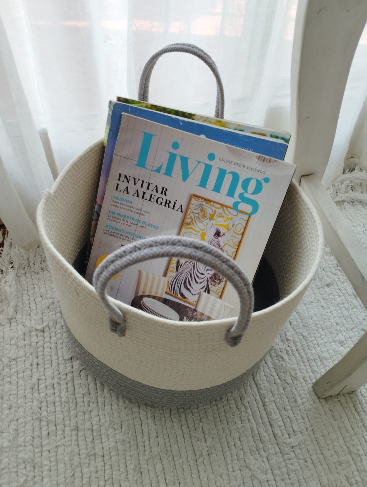 Revistero blanco con una revista “Living”, junto a una silla blanca en una habitación luminosa.