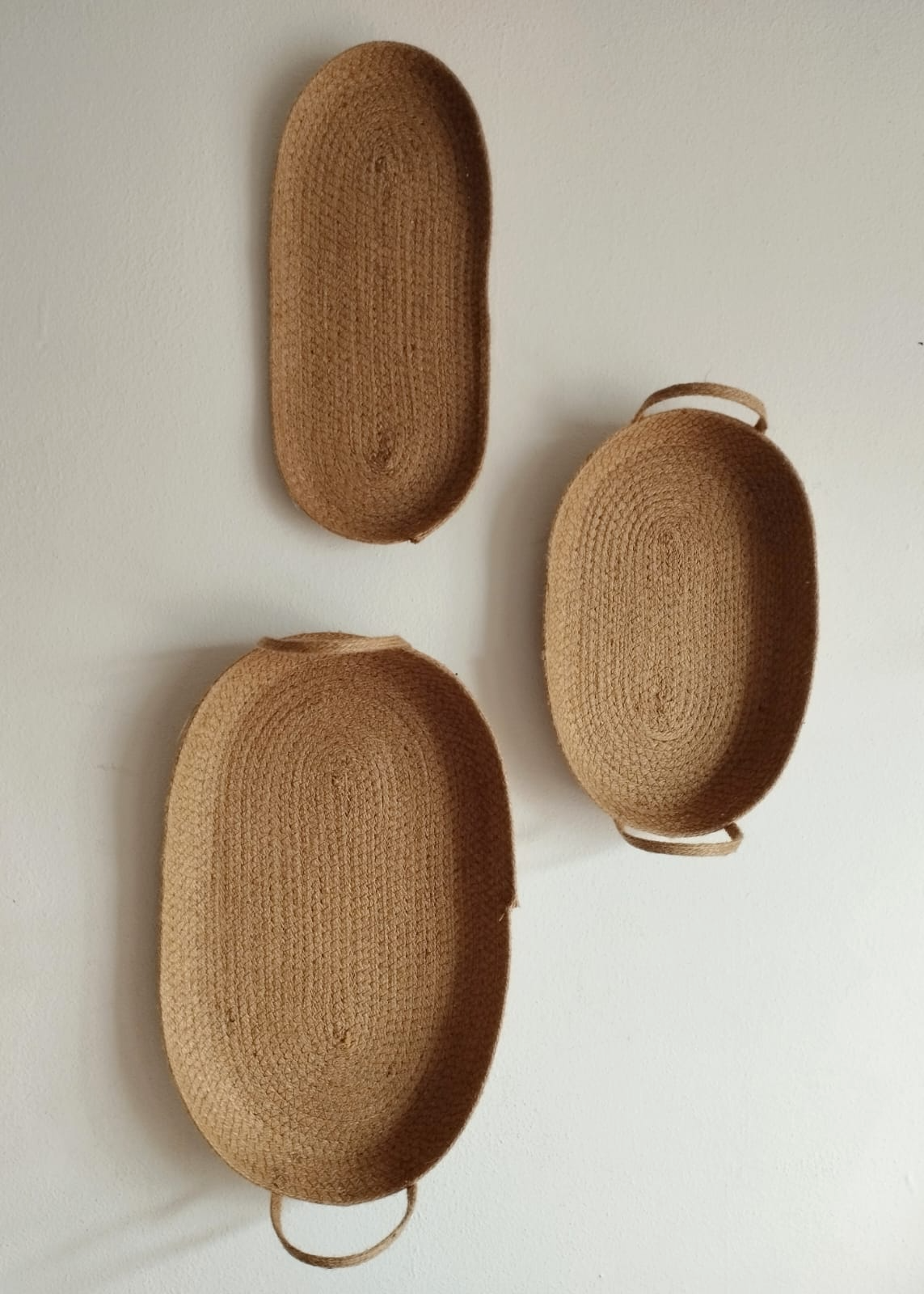 Tres bandejas de paja tejida apiladas sobre una mesa clara frente a unas cortinas transparentes.