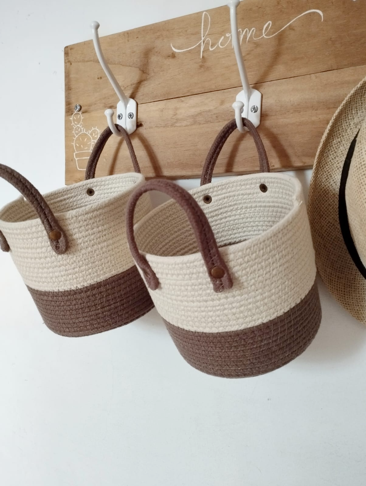 Tres cestas colgantes de mimbre y un sombrero de paja sobre una tabla de madera con ganchos.