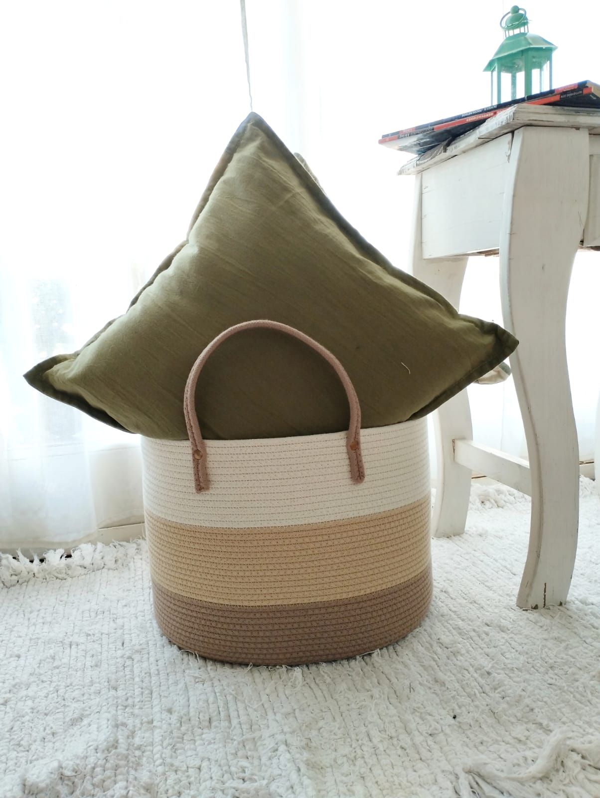 Cesta de mimbre con manta color crema junto a una mesa blanca en una habitación luminosa y espaciosa.