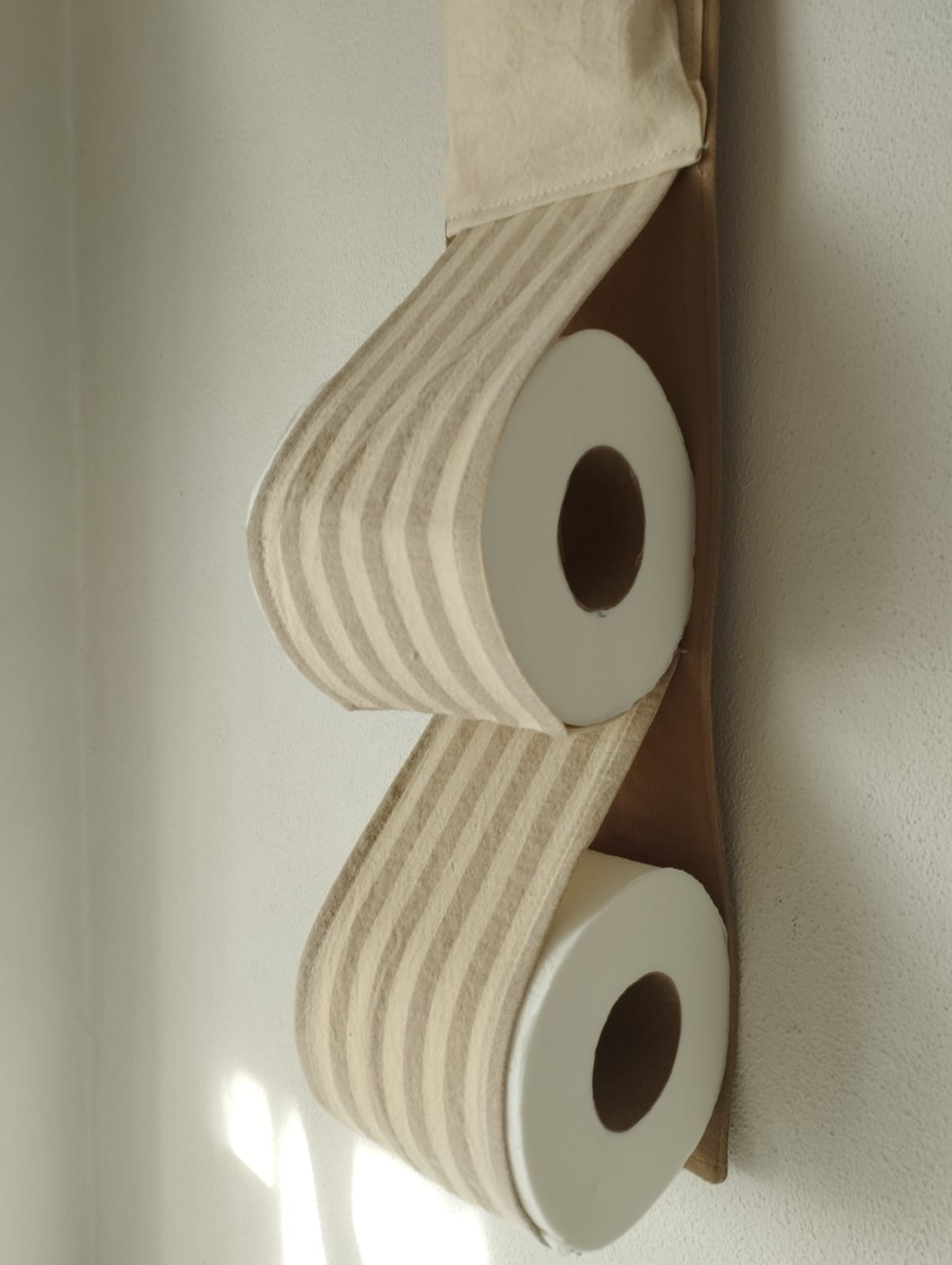 Dos rollos de papel higiénico blanco montados en un soporte de pared sobre una pared beige.