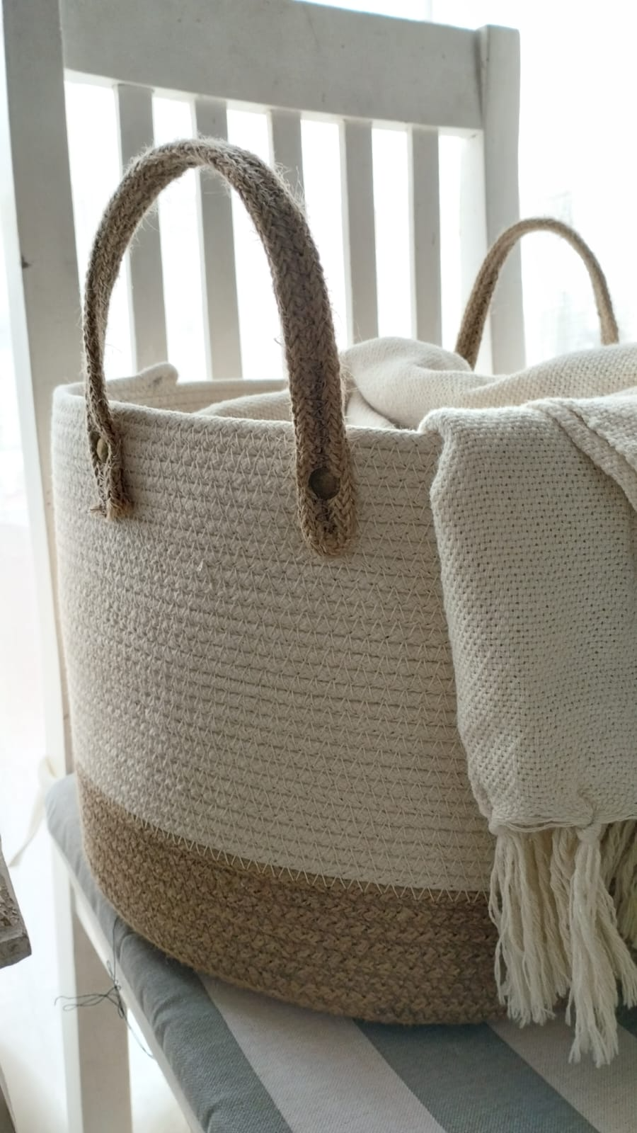Dos cestas de almacenamiento tejidas de color beige apiladas junto a una ventana luminosa.