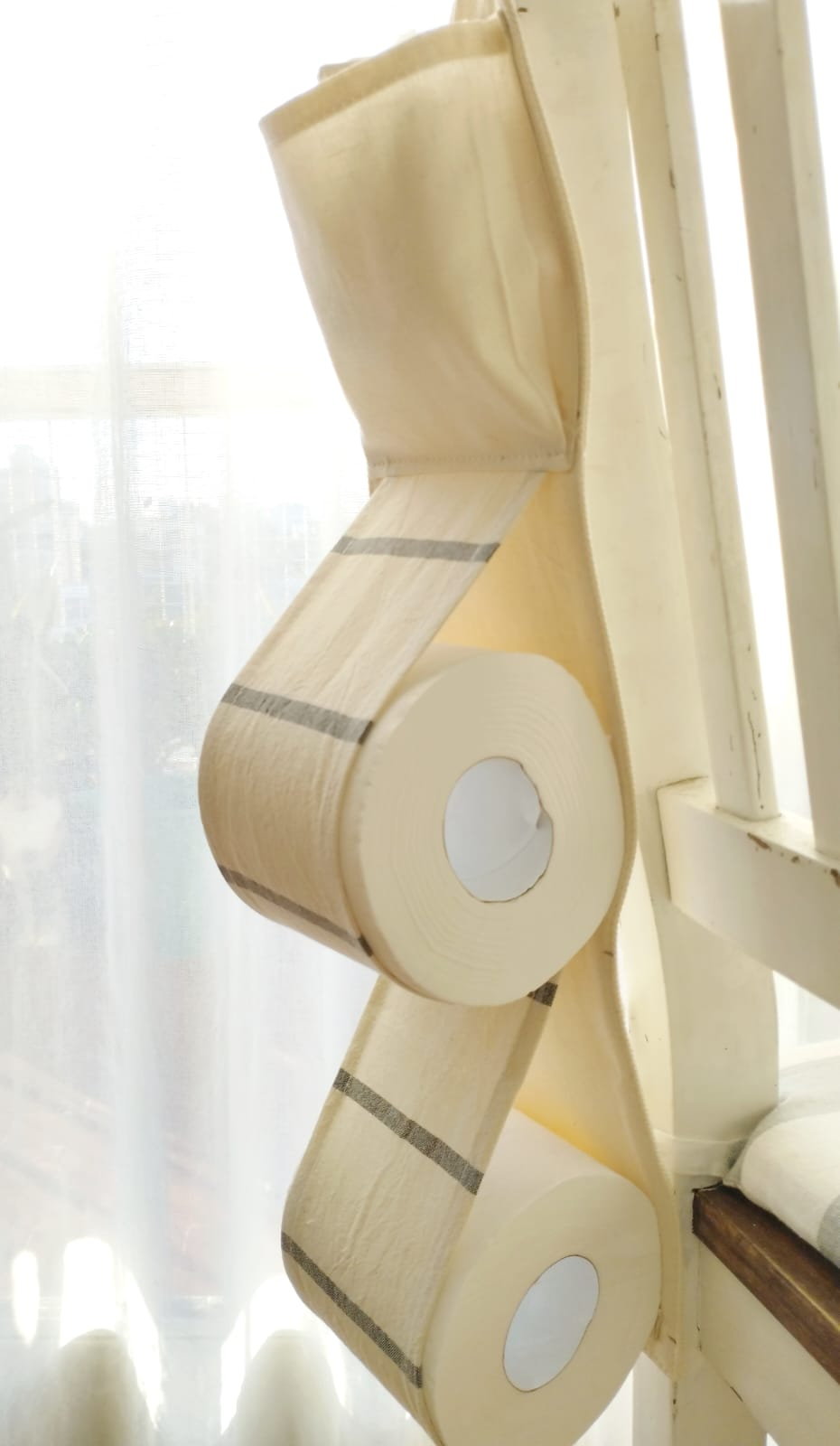 Rollos de papel higiénico beige apilados colgando de un sujetador de cortina.