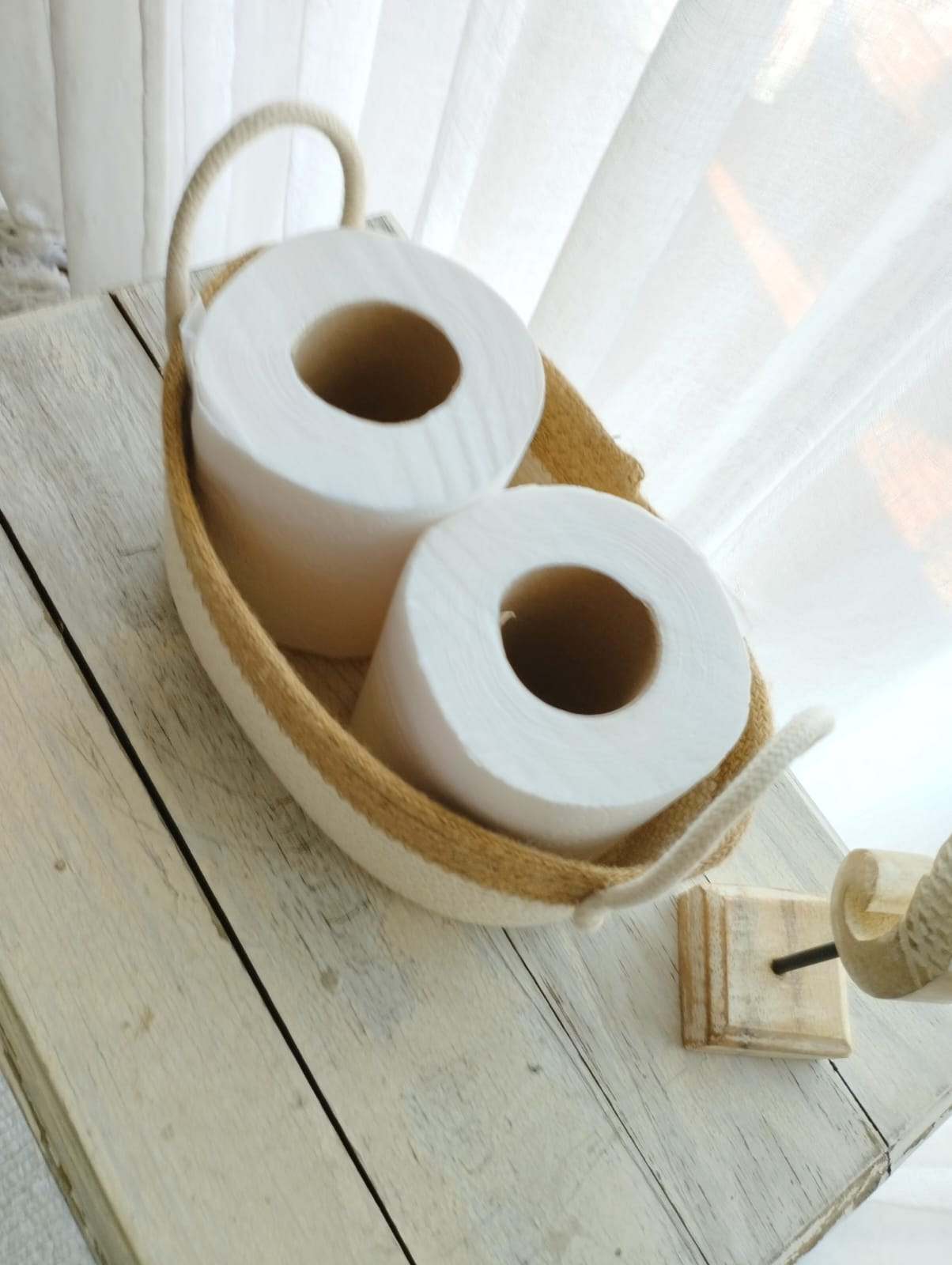 Cesta tejida bicolor con asas de cuerda y adorno de caballito de mar sobre una mesa rústica blanca.