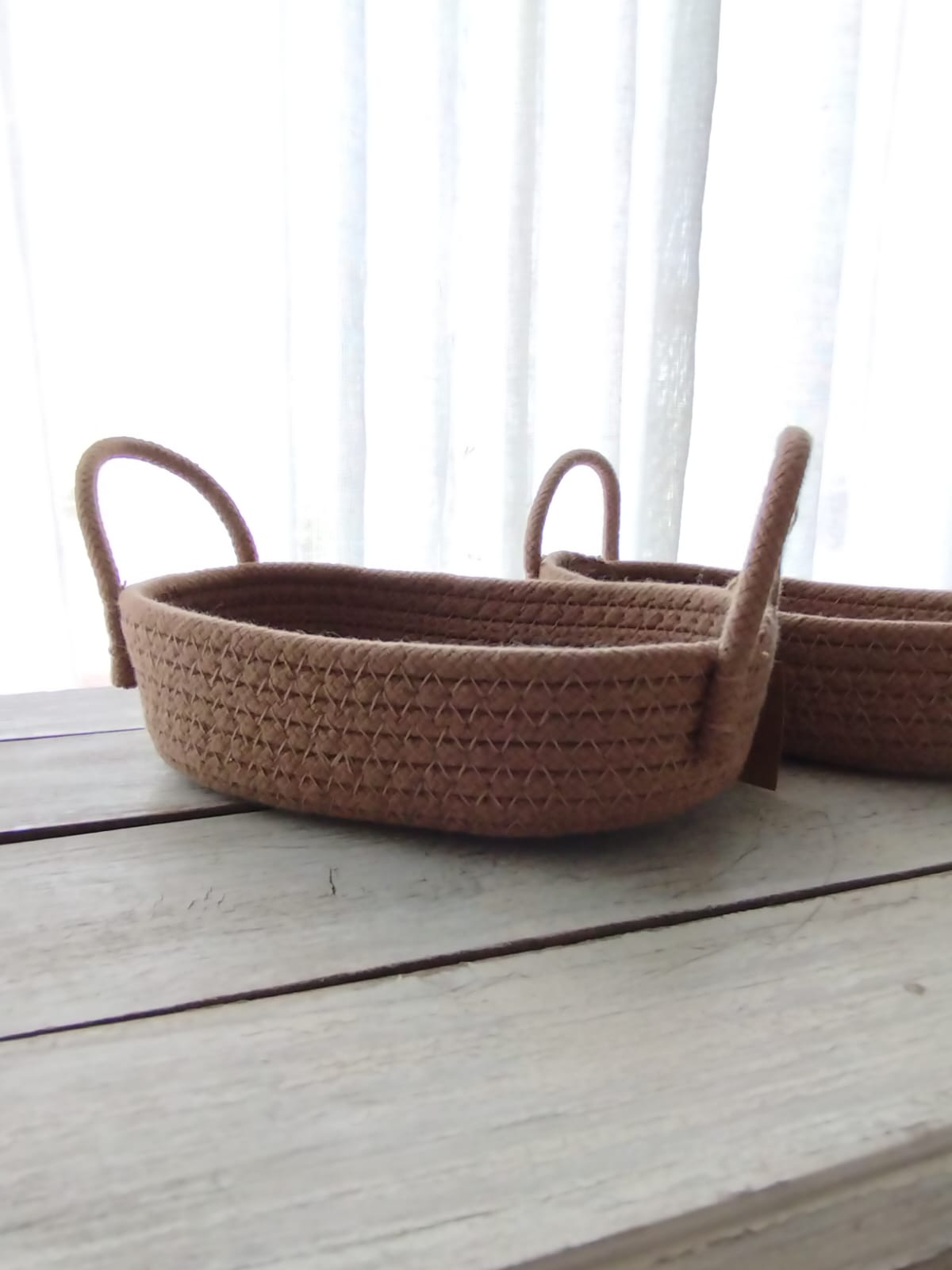 Cesta tejida con un asa en relieve sobre una mesa de madera blanca junto a una ventana luminosa.