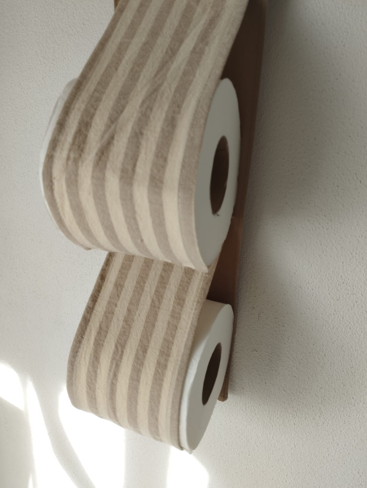 Dos rollos de papel higiénico blanco montados en un soporte de pared sobre una pared beige.