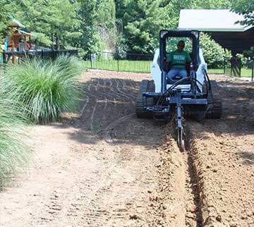 A man operating a trencher digging a line in a yard.