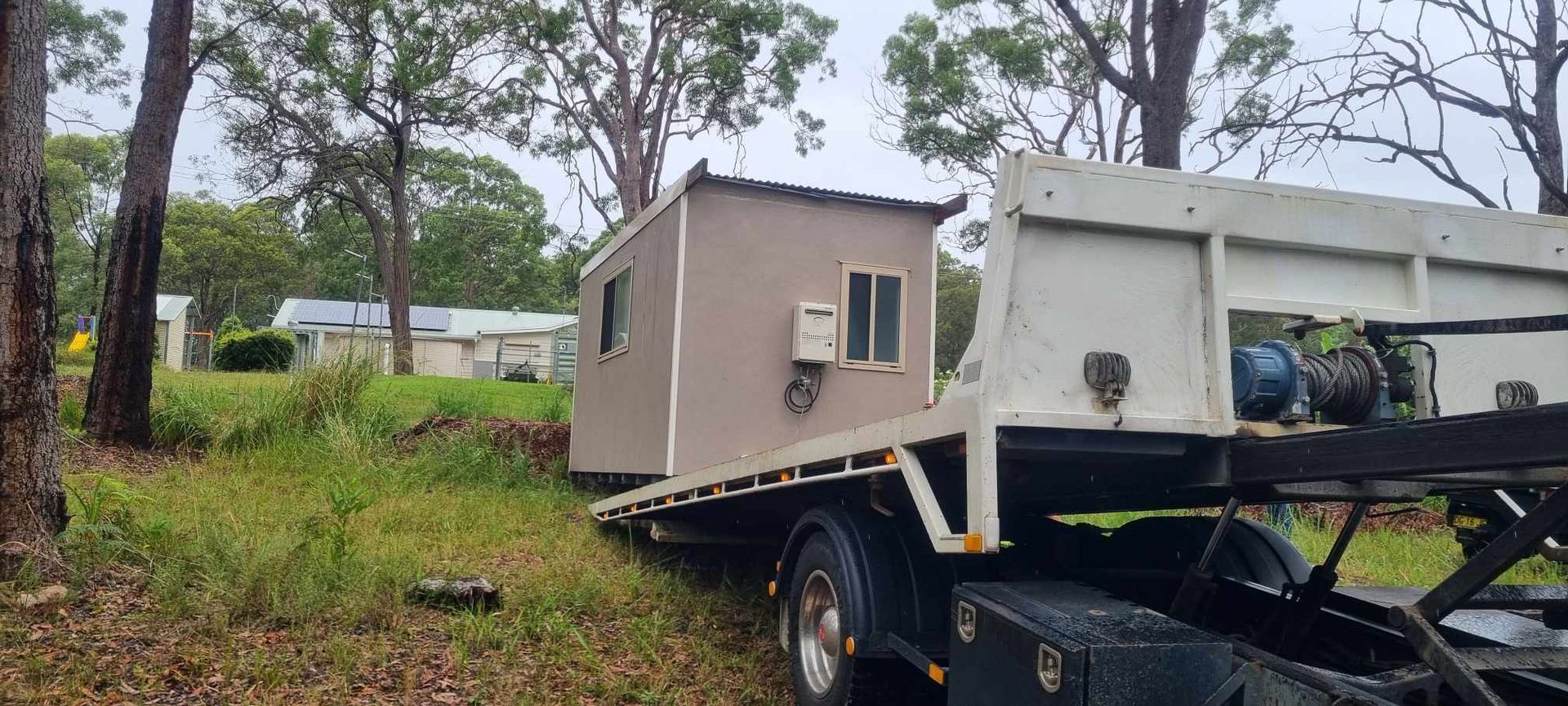 A tow truck is carrying a small house on the back of it. — A Towing Service In Forster, NSW