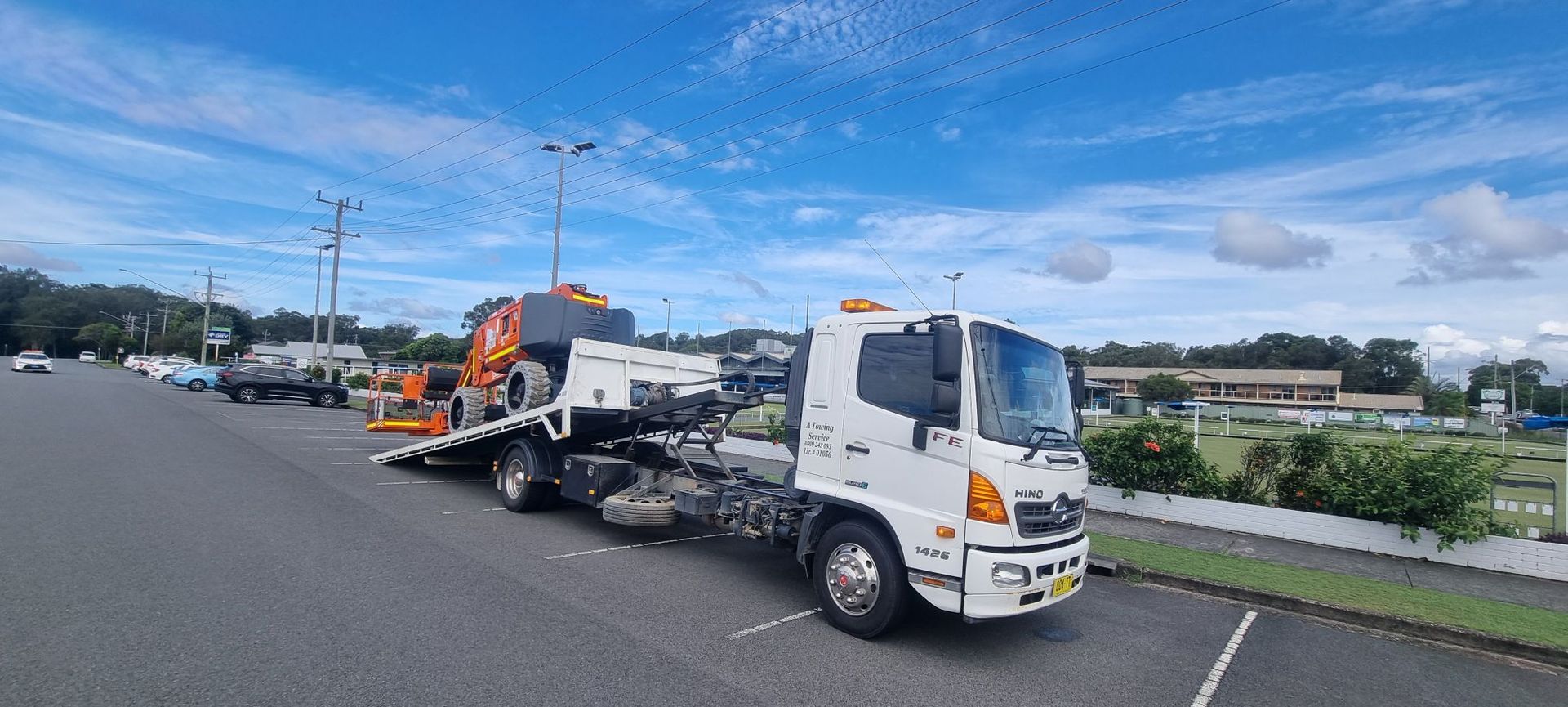 A White Tow Truck on an Asphalt Surface Under a Partly Cloudy Sky — A Towing Service In Seal Rocks, NSW