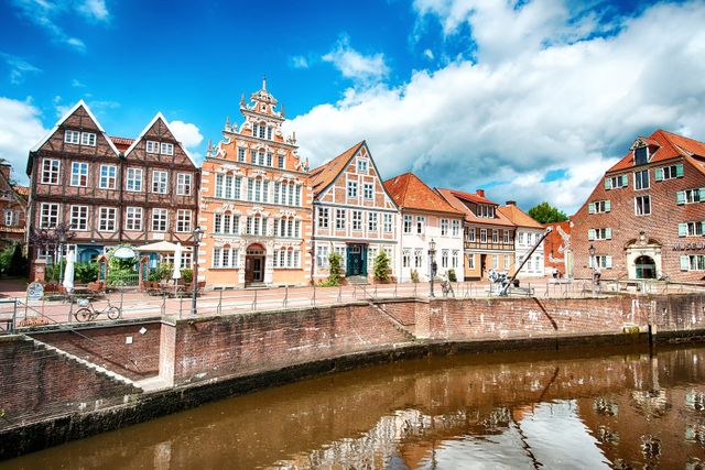 Historische Gebäude am Flussufer mit roten Dächern und ein Kanal unter einem bewölkten Himmel
