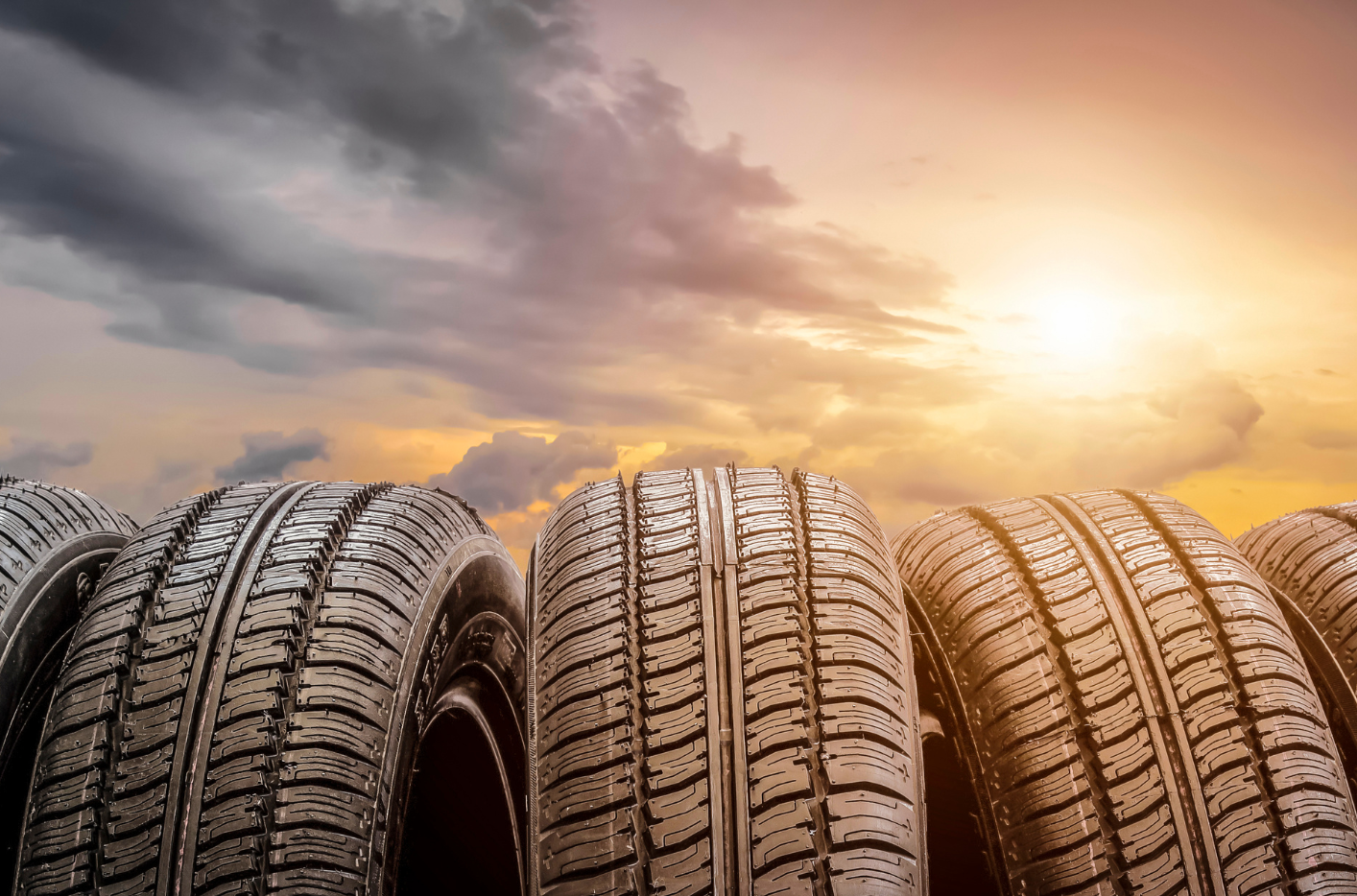 A row of tires stacked on top of each other in front of a cloudy sky at sunset.