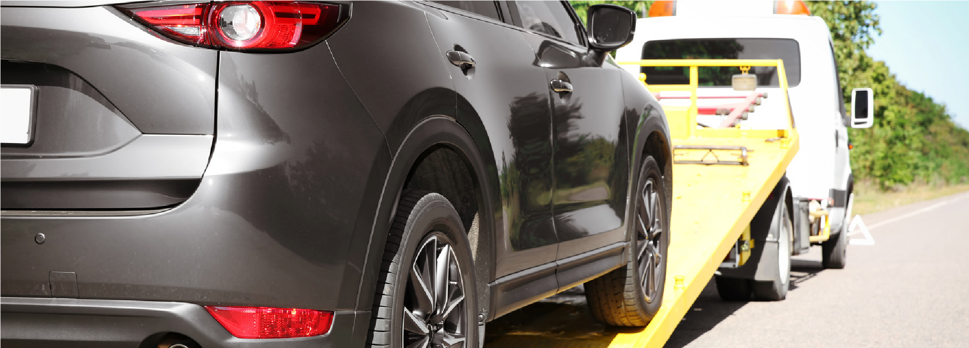 A dark SUV is being towed by a yellow flatbed tow truck on a road.