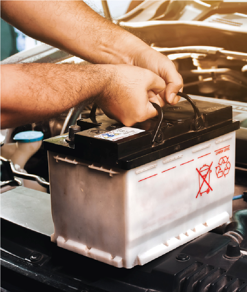 Hands installing a car battery in an engine compartment
