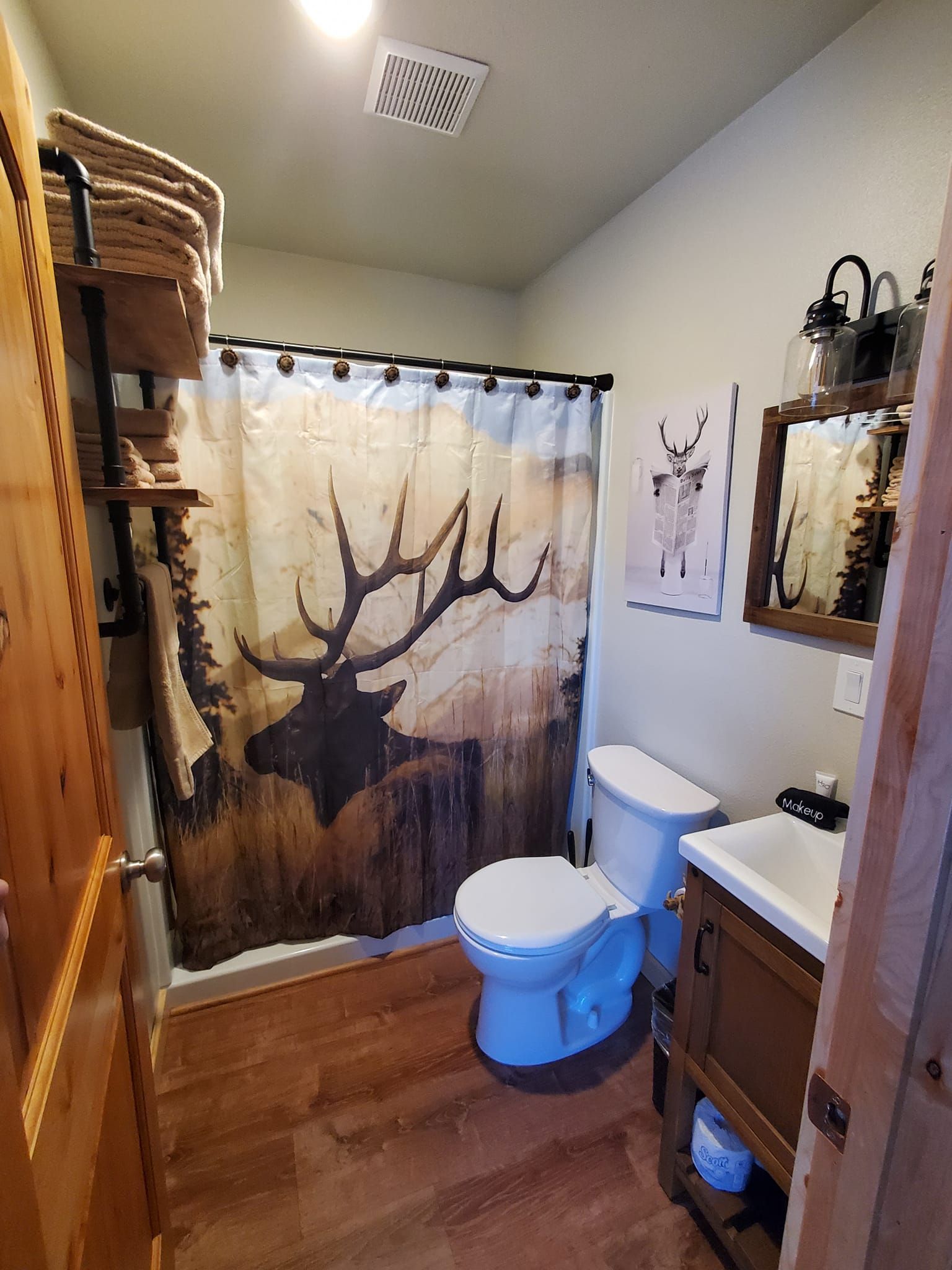 A bathroom with a toilet , sink and shower curtain with a deer on it.