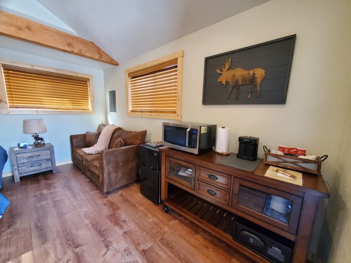 A living room with a couch , microwave , coffee maker and a moose painting on the wall.