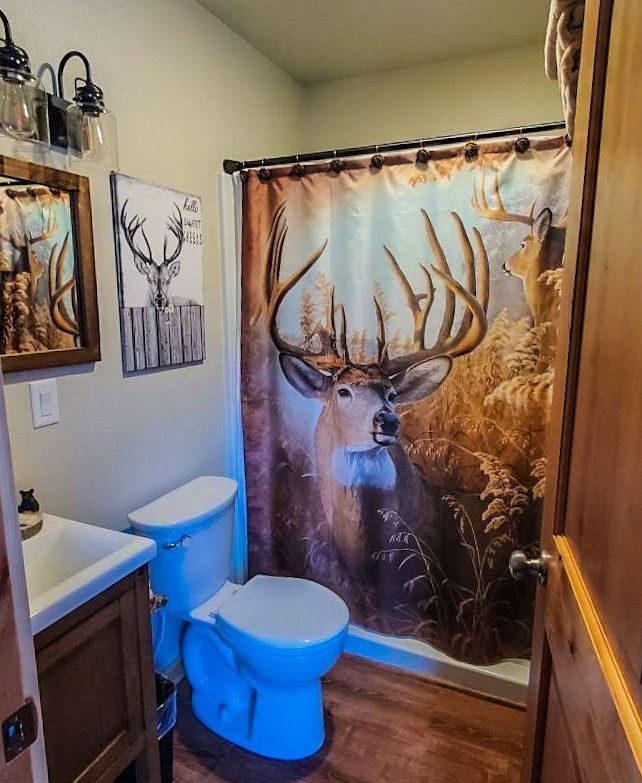 A bathroom with a toilet , sink and shower with a deer shower curtain.