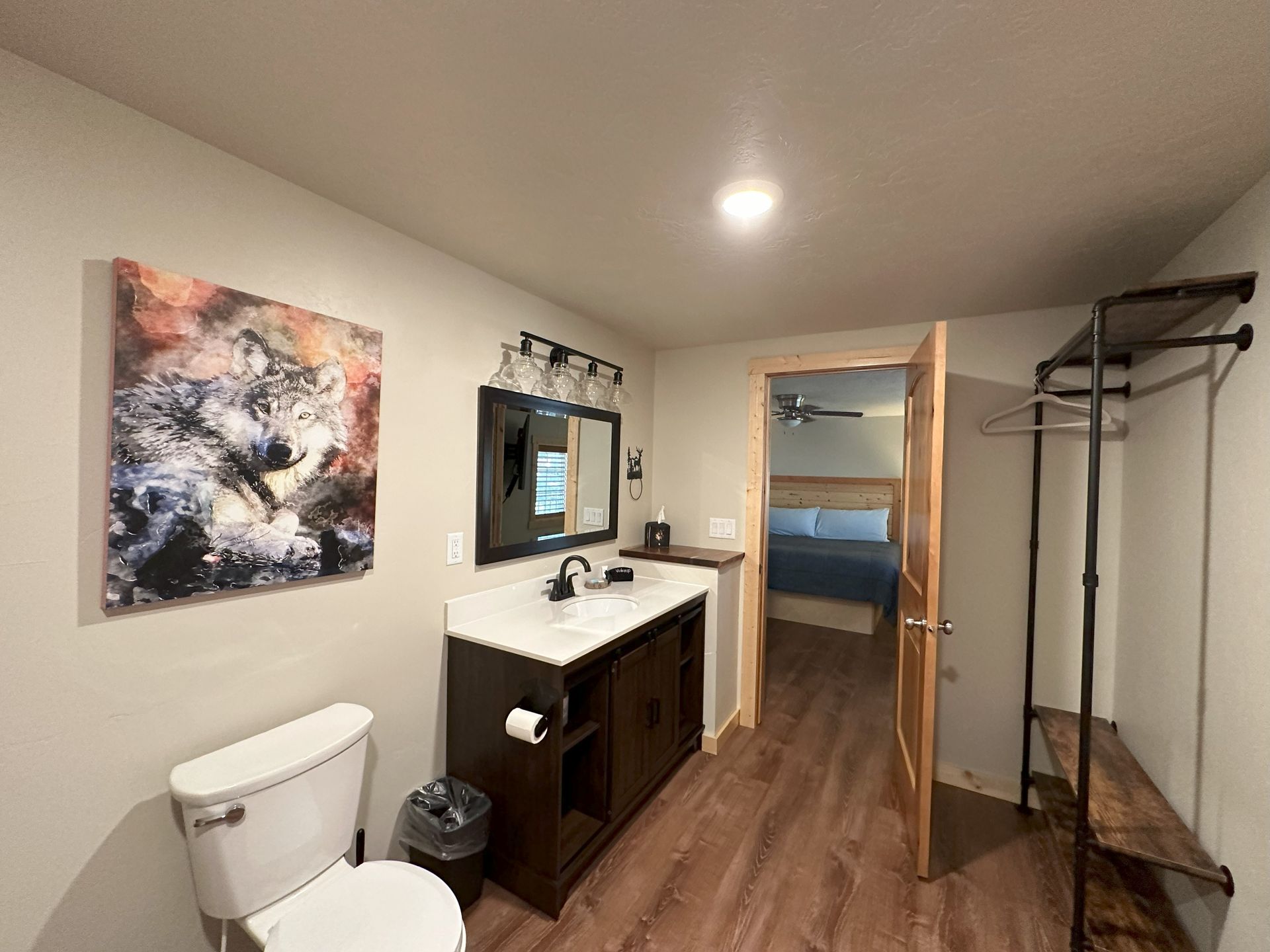 A bathroom with a toilet , sink , mirror and painting on the wall.