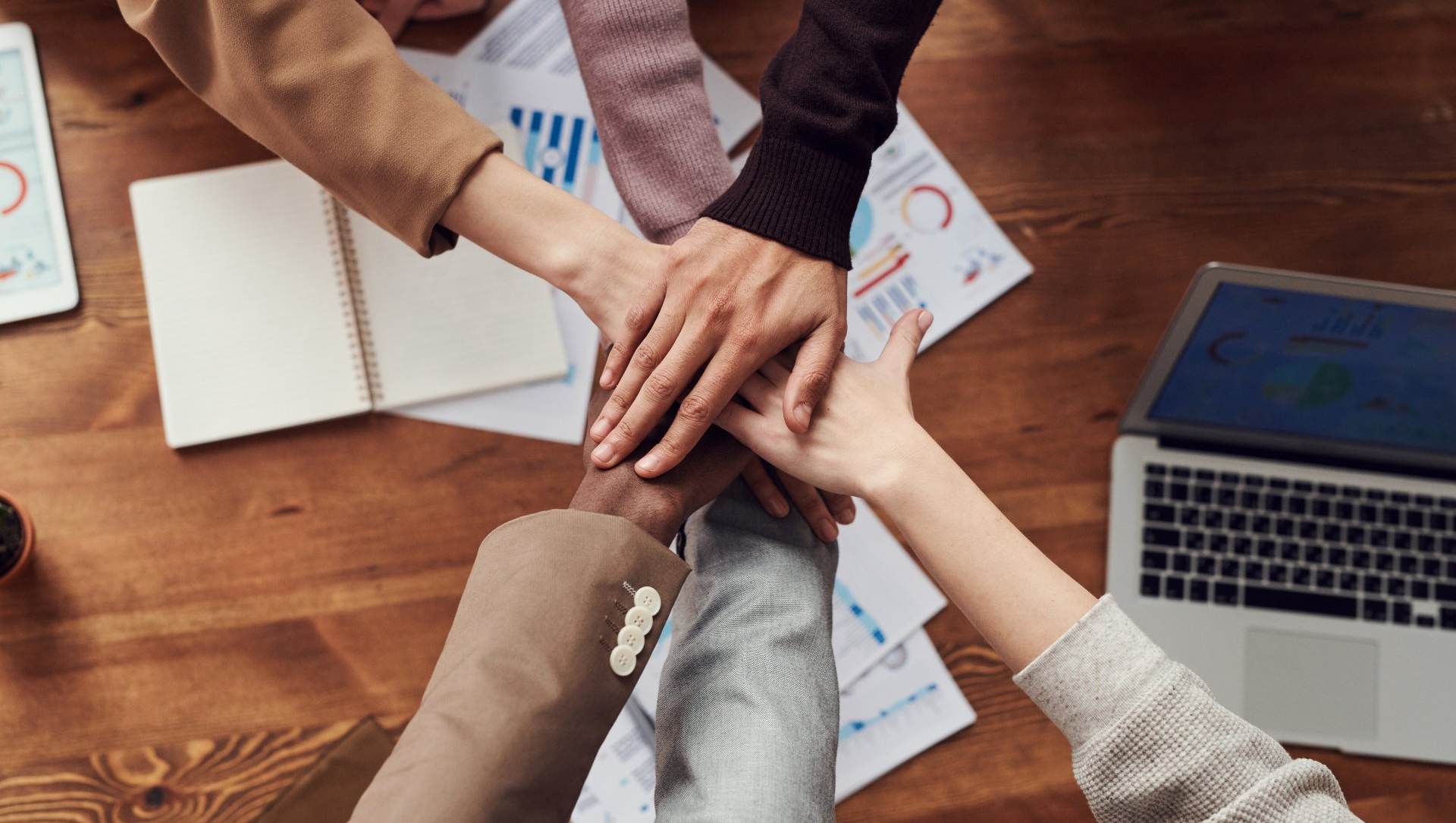 A group of people are putting their hands together on a wooden table.