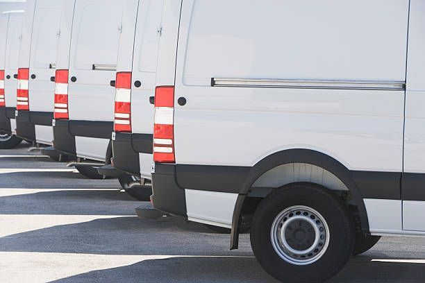 White delivery vans parked in a row, rear view showing taillights and tires.