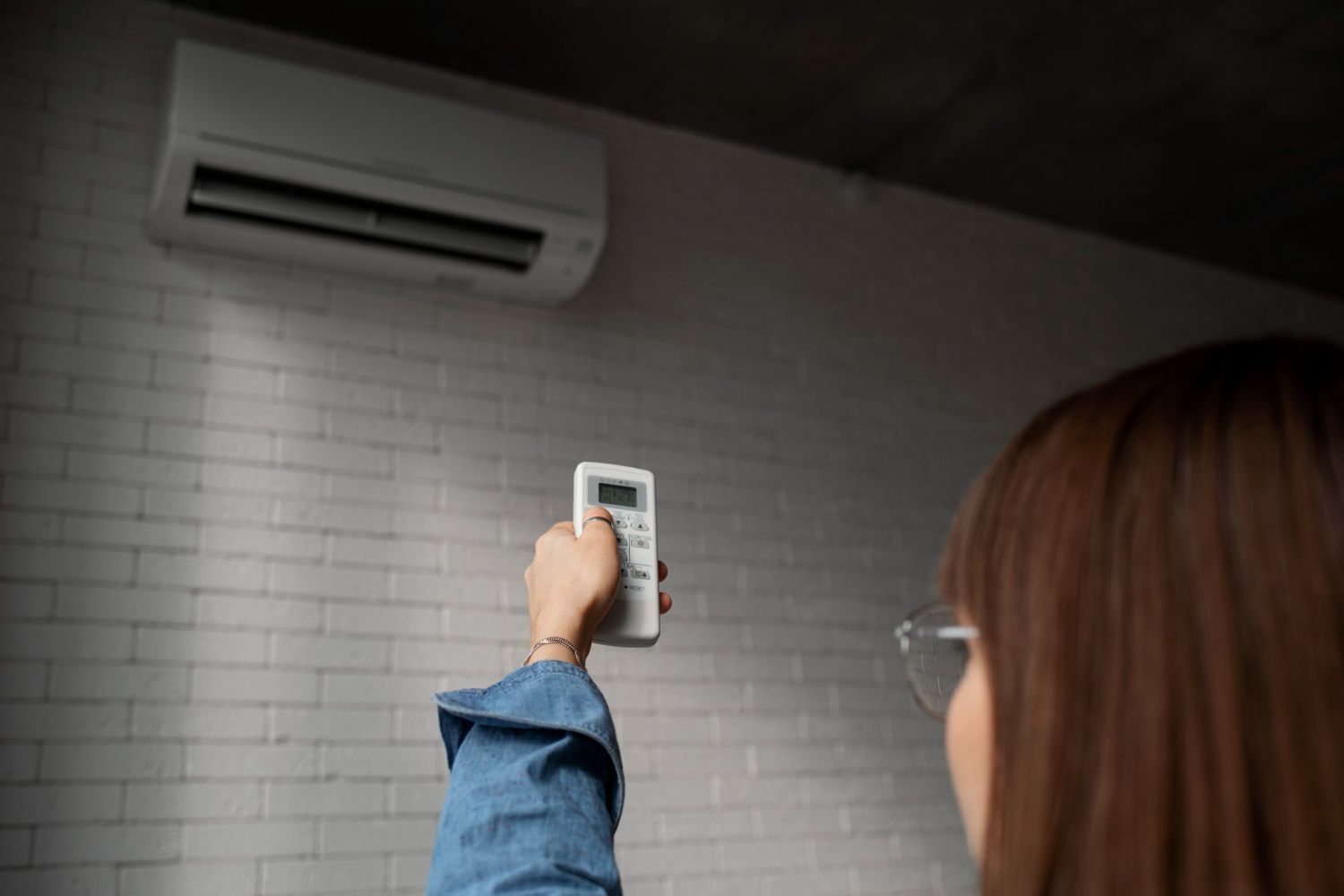 Hand holding a remote toward a wall-mounted air conditioner in a tiled room