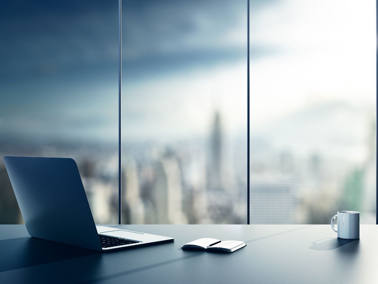 Um laptop está sobre uma mesa em frente a uma janela.