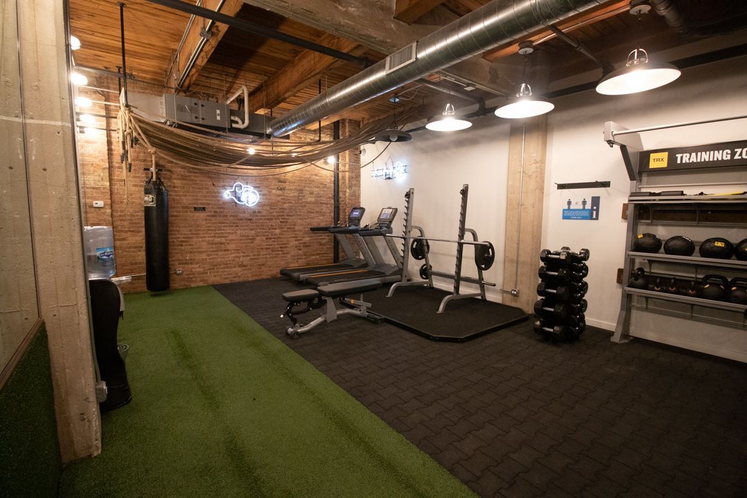 A gym with a treadmill , bench , and dumbbells at The Lofts at Gin Alley.