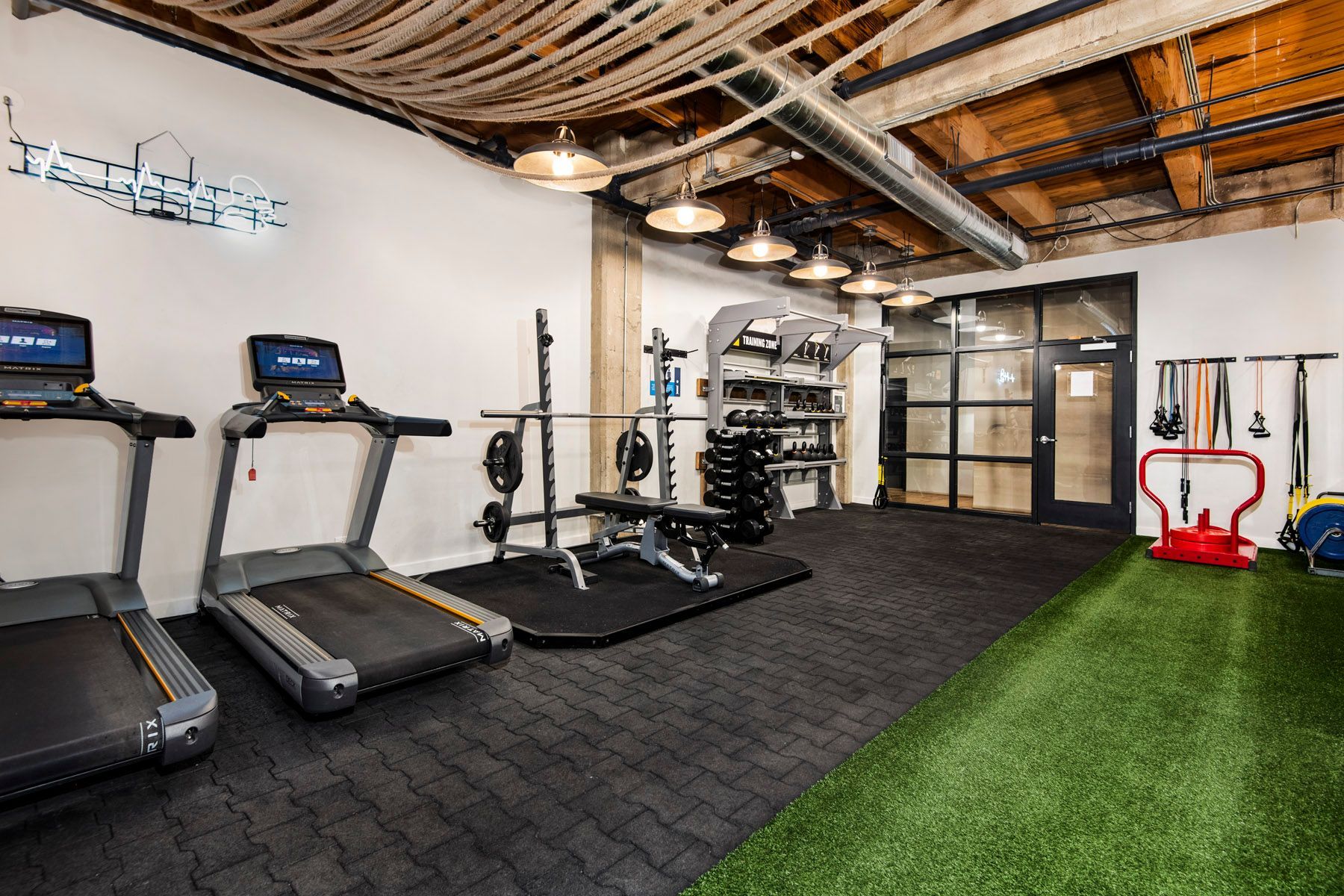 A gym with treadmills , weights , and a green carpet at The Lofts at Gin Alley.