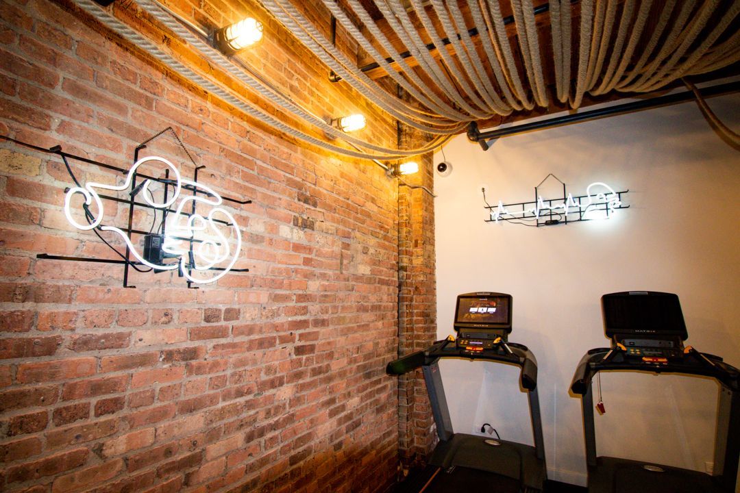 A room with two treadmills and a neon sign on the wall at The Lofts at Gin Alley.