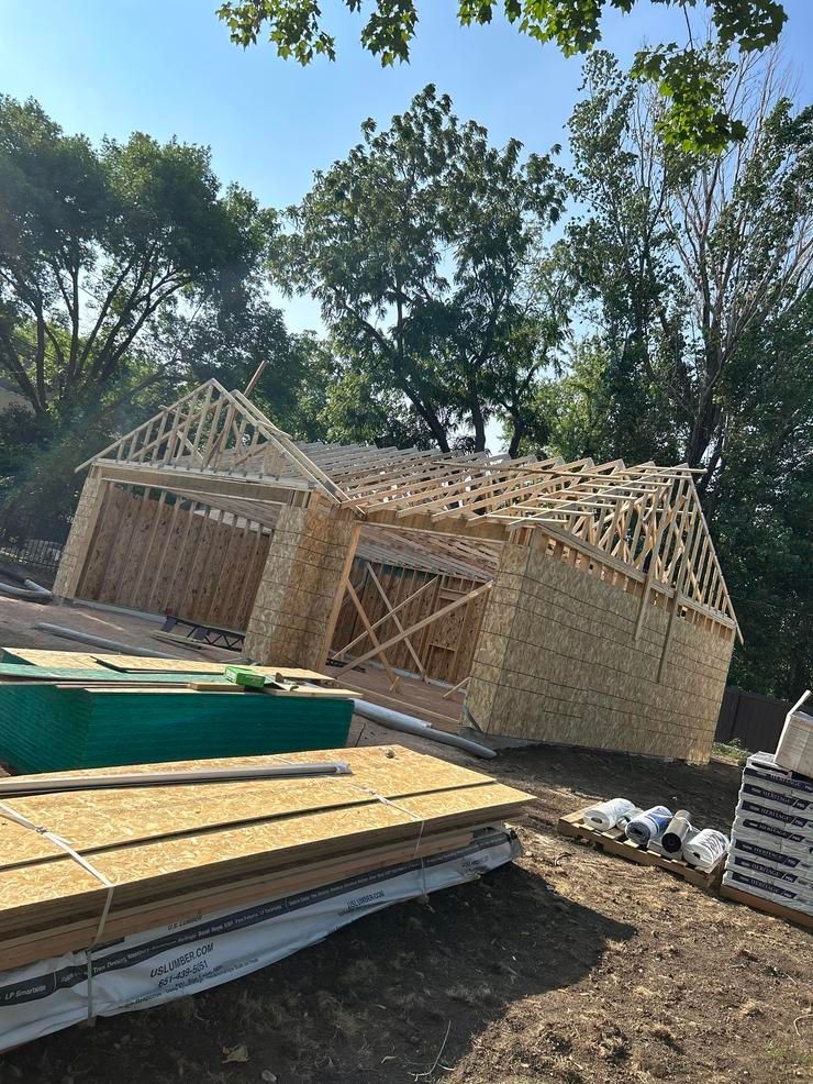 A wooden garage is being built in a yard with trees in the background.