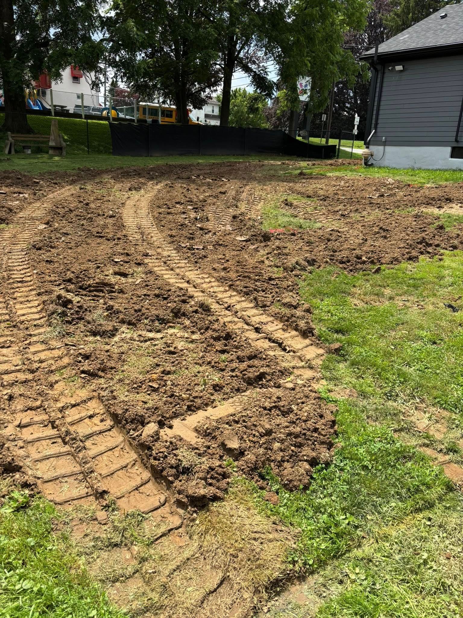 A muddy, churned-up yard with tractor tracks; some green grass.